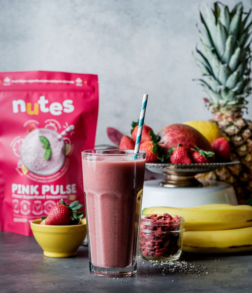Nutes pink pulse superfood smoothie in a glass with package and fruit in background