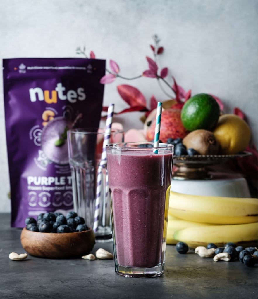Nutes purple tonic superfood smoothie in a glass with package and fruit in background